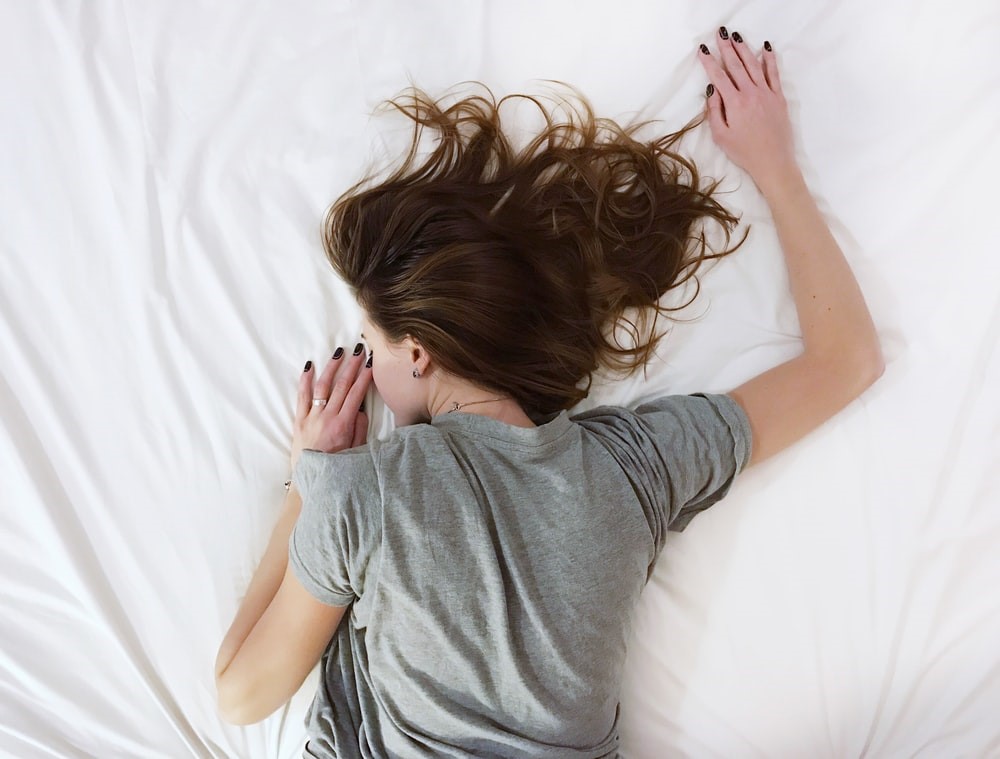 girl in grey shirt lying on white sheets
