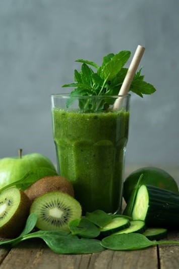 A green smoothie blended with vegetables and fruits like kiwis, apples, and cucumbers.