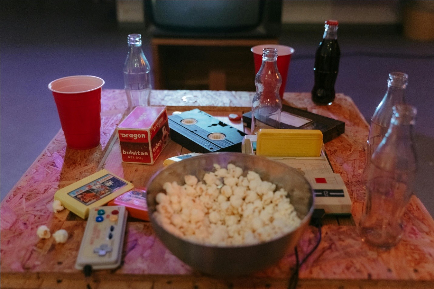 bowl of popcorn, empty soda bottles, and cups on table