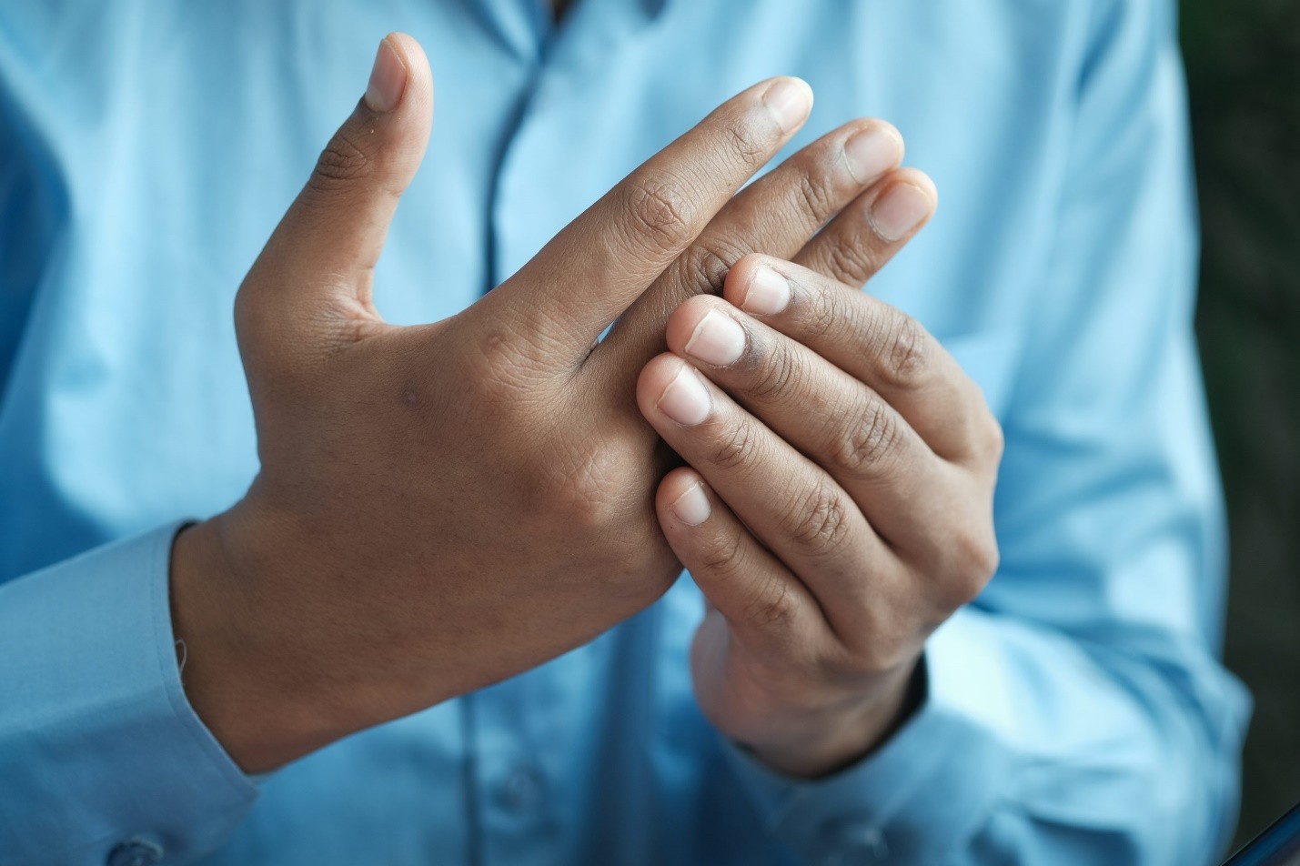 A closeup of a person holding his fingers with the other hand due to pain
