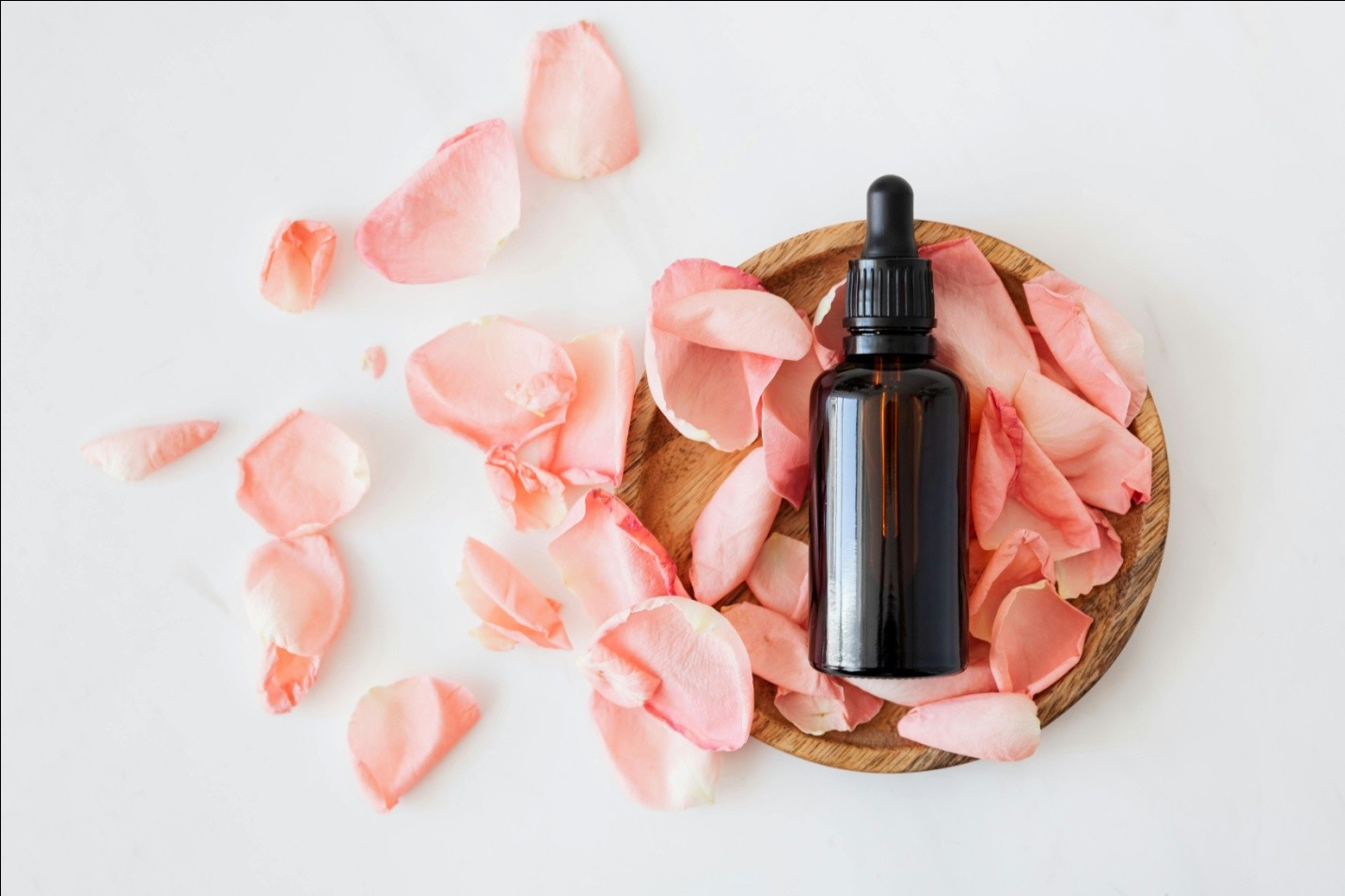an amber bottle with pink petals on a wooden plate