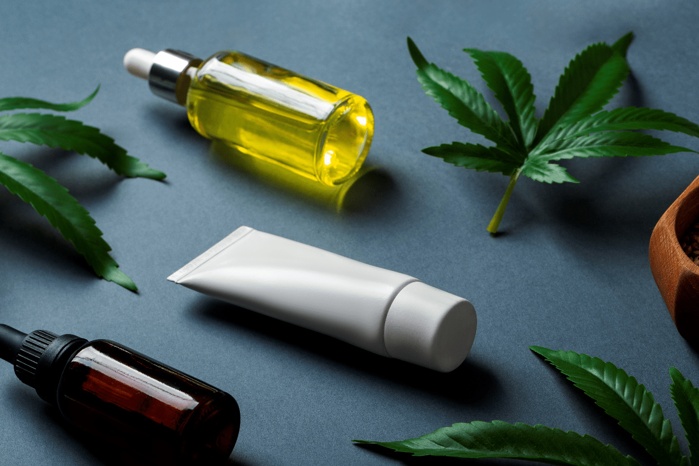 dropper bottles, a tube, and some leaves on a blue surface