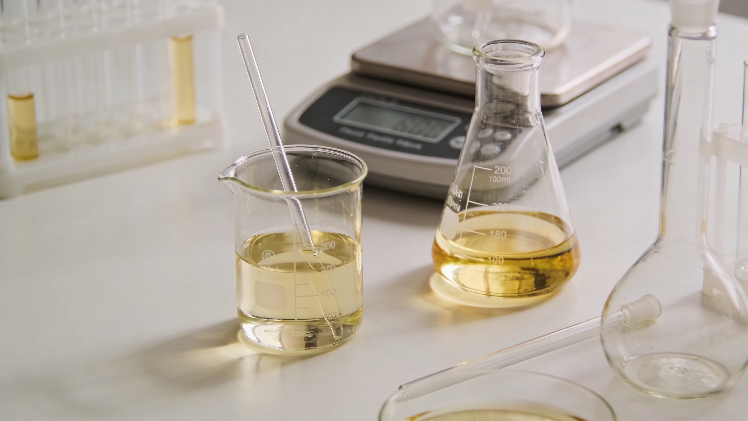 Scientific laboratory equipment including beakers and flasks filled with yellow liquid for testing chemical substances.