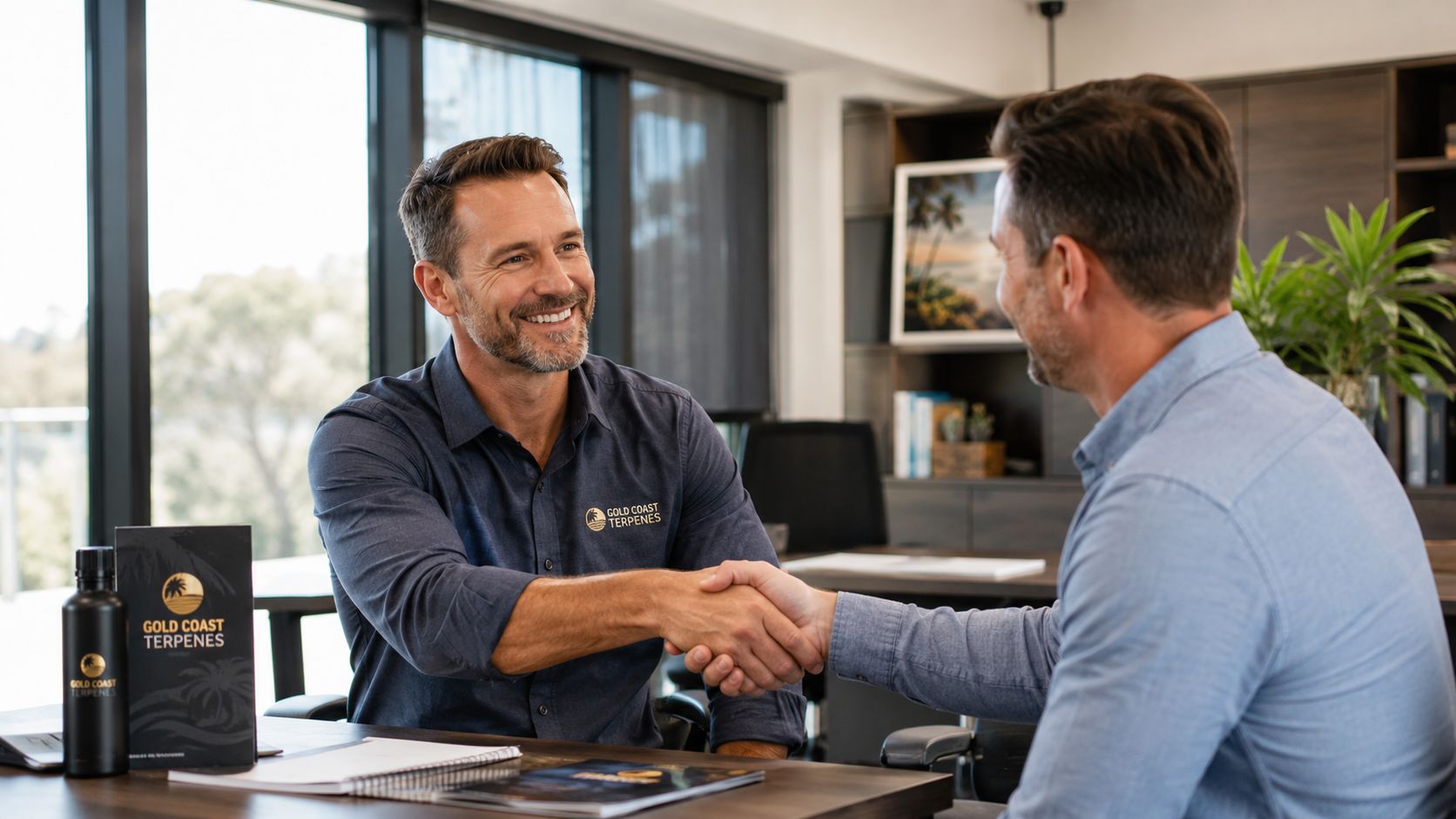 Two professional men shaking hands across an office desk with Gold Coast Terpenes branding in the foreground.