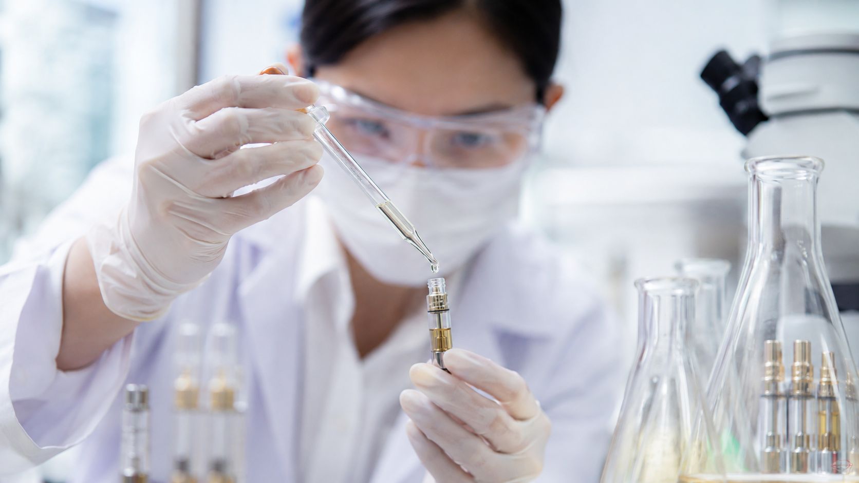 A female scientist in a lab coat using a dropper to fill a vape cartridge with oil.