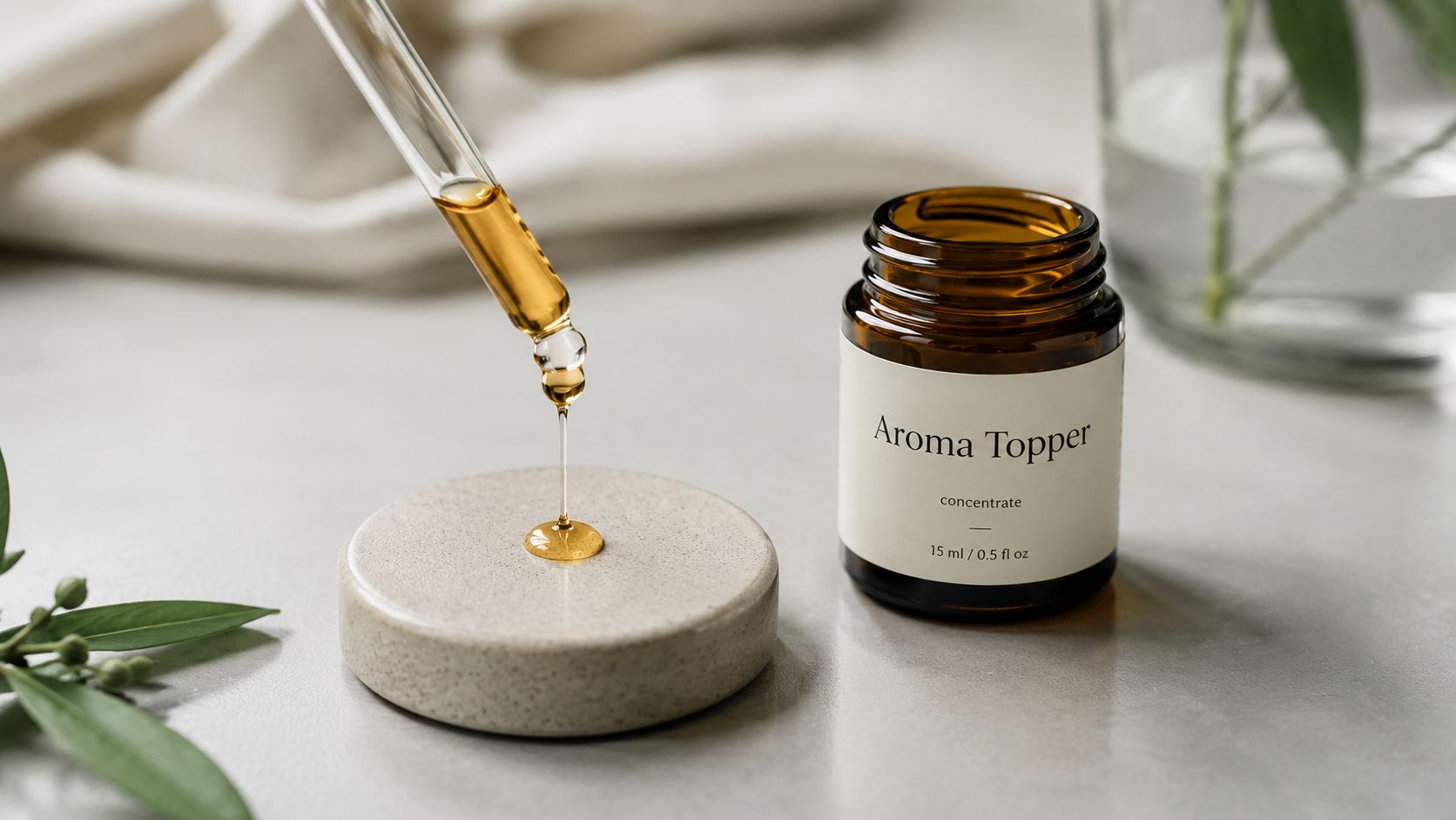 A glass dropper dispensing golden essential oil onto a small stone surface next to an amber bottle.